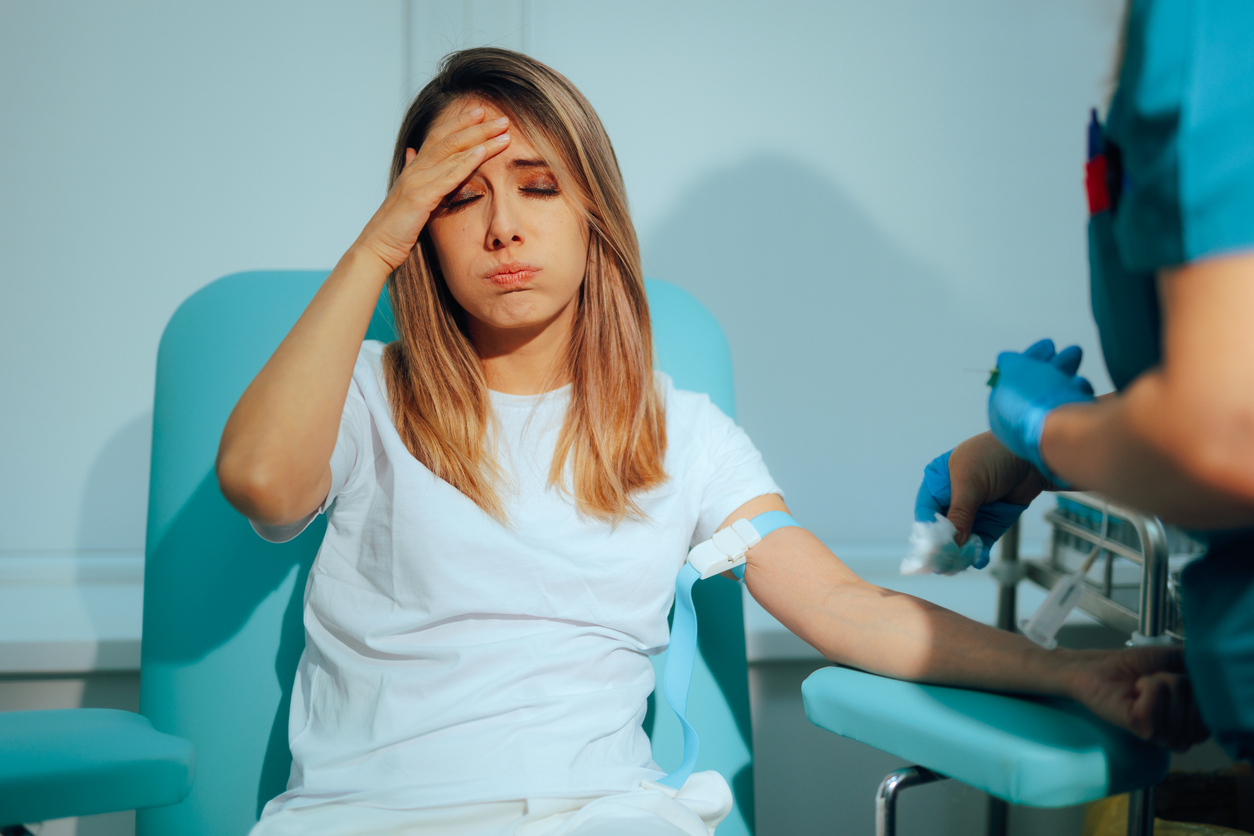 Nervous woman covering her face while a gloved nurse prepares her arm for an IV, illustrating fear of needles